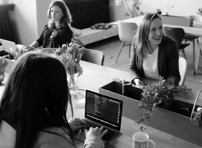 Three girls in an office working at their computers, one of them smiling.